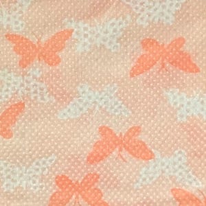 May include: A close-up of a peach-colored fabric with a repeating pattern of butterflies. The butterflies are in two colors: peach and white. The fabric has a textured, dotted appearance.