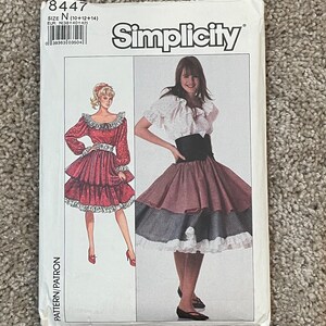May include: Simplicity sewing pattern number 8447 for sizes 10, 12, and 14. The pattern includes instructions for making two dresses. One dress is a red and white polka dot dress with a ruffled skirt. The other dress is a white blouse with a brown and white plaid skirt.