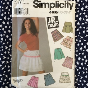 May include: Simplicity sewing pattern for Jr. Trend skirts. The pattern features various skirt styles, including pleated, tiered, and pocketed designs. The package includes a photo of a woman wearing a white skirt with a red gingham trim. The pattern size is AA 3/4-9/10.