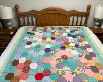 Puede incluir: Un edredón hecho a mano con un diseño de patchwork colorido de formas hexagonales. El edredón presenta una variedad de telas en tonos de azul, rosa, morado, amarillo y rojo. El edredón está colocado sobre una cama con un cabecero de madera y lámparas de noche.