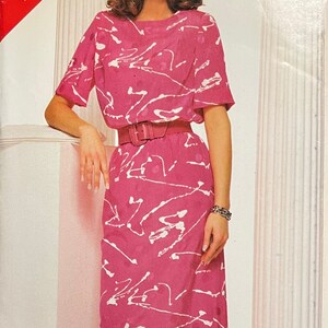 May include: A pink dress with a white abstract pattern and a red belt. The dress has short sleeves and a knee-length skirt.
