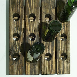 May include: A rustic wooden wine rack with multiple bottle slots. The rack is stained dark brown and has a distressed look. Three green glass wine bottles are partially visible in the slots.