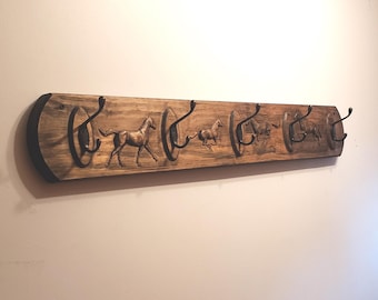 May include: Wooden coat rack with five hooks, each shaped like a horse's head. The rack is stained a dark brown and has a rustic look.