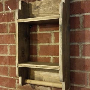 May include: A rustic wooden wall shelf with two shelves and a towel bar. The shelf is stained a dark brown color and has a distressed finish. The towel bar is made of natural wood.
