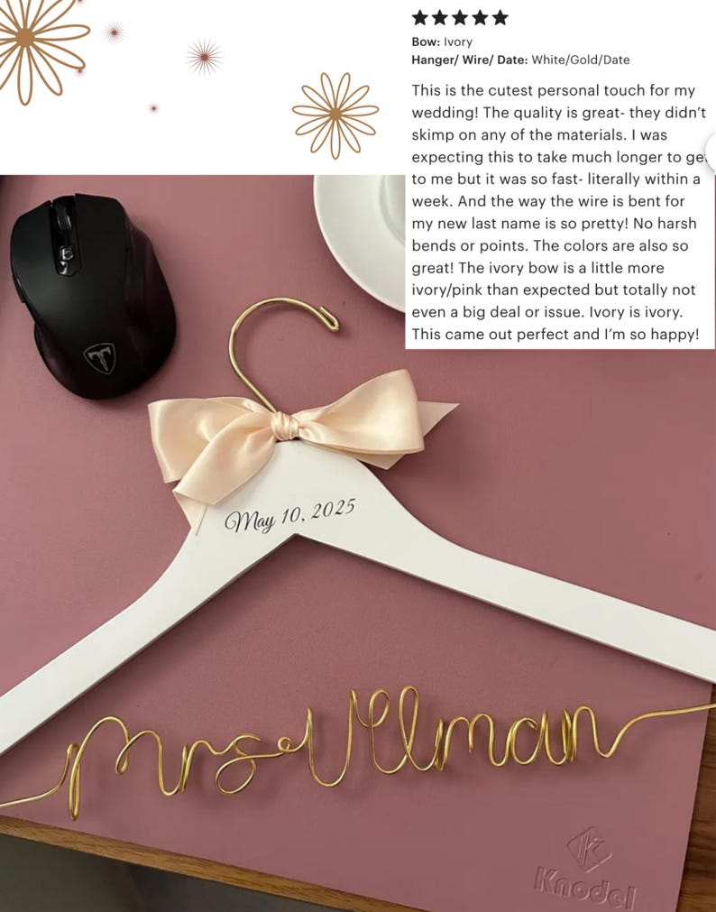 May include: A white wooden wedding dress hanger with a cream-colored bow and gold wire name. The date "May 10, 2025" is printed on the hanger. The wire spells out "Mrs. Vilman".