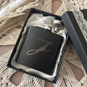 May include: Black flask with a silver funnel and a personalized engraved letter Z with a floral design. The flask is in a black box with a satin lining.