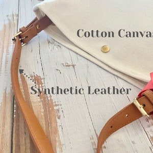 May include: A cream cotton canvas bag with a brown synthetic leather strap and gold-coloured hardware. The bag features a simple design with a flap closure and a button. The words "Cotton Canvas" and "Synthetic Leather" are visible.