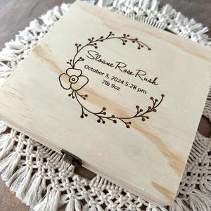 May include: A light wood keepsake box with a floral design and the inscription "Sloane Rose Rush, October 3, 2024 5:28 pm, 7lb 9oz".