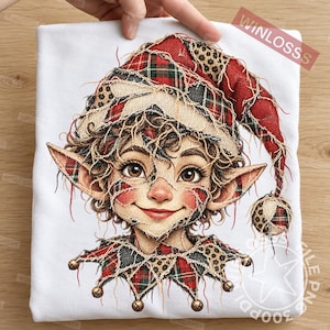 Op de afbeelding: Een wit t-shirt met een grafische print van een elf met grote oren, die een muts en kraag draagt van rood, groen en zwart ruitjespatroon en luipaardprint. De tekst WINLOSSS staat in de rechterbovenhoek gedrukt.