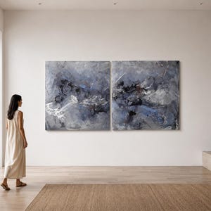 Puede incluir: Un conjunto de arte mural díptico que presenta dos grandes lienzos cuadrados con pinceladas abstractas en tonos gris carbón, azul pizarra y blanco. La aplicación de pintura texturizada crea una composición estratificada.