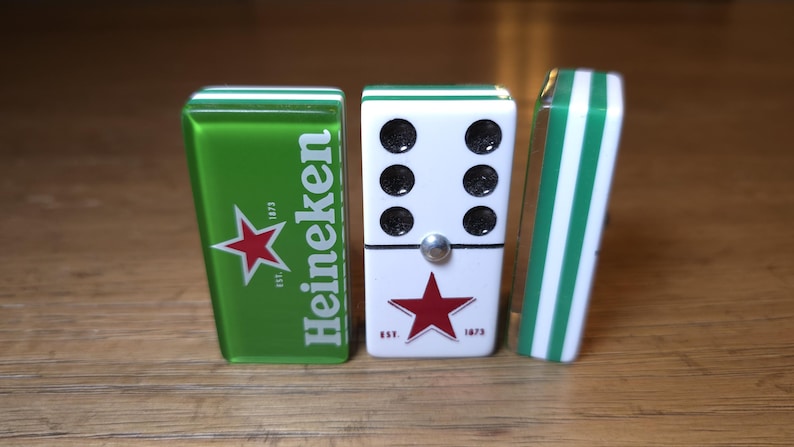 Op de afbeelding: Dominoset met een groen en wit thema. E&eacute;n domino heeft het Heineken-logo met een rode ster. De middelste domino is wit met zwarte stippen en een rode ster. De derde domino heeft groen-witte strepen.