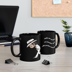 May include: Black ceramic mug featuring a cartoon illustration of a person in a white suit and hat, with a downward gaze. The mug on the right has the text "Annie, are you okay? Are you okay, Annie? ...did you have your coffee?"