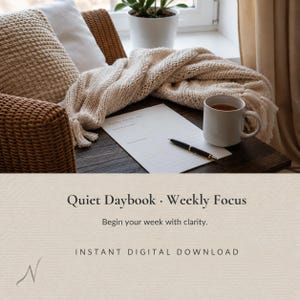 May include: A white paper sheet titled Weekly Focus with lined sections for notes, a black ballpoint pen, a white ceramic mug filled with tea, a beige knit throw blanket, and a textured beige pillow on a dark wooden surface.