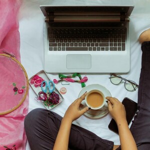 K&ouml;nnte beinhalten: Ein Laptop, ein Stickrahmen und Bastelmaterialien sind auf einer wei&szlig;en Oberfl&auml;che angeordnet. Eine Tasse Kaffee steht in der N&auml;he einer Brille und eines Smartphones. Die Szene deutet auf einen kreativen Arbeitsplatz hin.