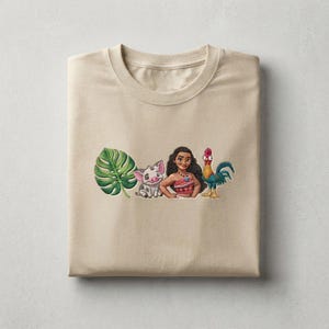 May include: A beige crew neck t-shirt featuring a central embroidered graphic. The design includes a large green monstera leaf, a small grey piglet, a cartoon character with long dark hair wearing a patterned top, and a colorful rooster.