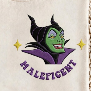 Puede incluir: Dise&ntilde;o bordado de color crema con Mal&eacute;fica con piel verde, cuernos negros y un cuello morado. La palabra "MAL&Eacute;FICA" est&aacute; bordada en escritura morada debajo del personaje, con dos estrellas amarillas a cada lado.