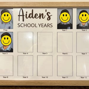 May include: A light wood-framed photo display board titled Aiden's SCHOOL YEARS in dark text. It features twelve rectangular slots for school portraits labelled from Prep to Year 12. Four slots contain photos with yellow smiley face stickers.