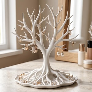 Peut inclure: Un présentoir à bijoux blanc en forme d'arbre avec des branches et des racines étendues. Les branches portent divers colliers, bagues et boucles d'oreilles en or et en argent, tandis que le plateau de base contient des bagues supplémentaires.