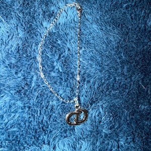 Puede incluir: Una pulsera de cadena de metal en tono plateado que presenta un dije colgante con las letras CD entrelazadas. La delicada cadena de eslabones incluye un peque&ntilde;o cierre de mosquet&oacute;n en el extremo para asegurar este accesorio de mu&ntilde;eca.