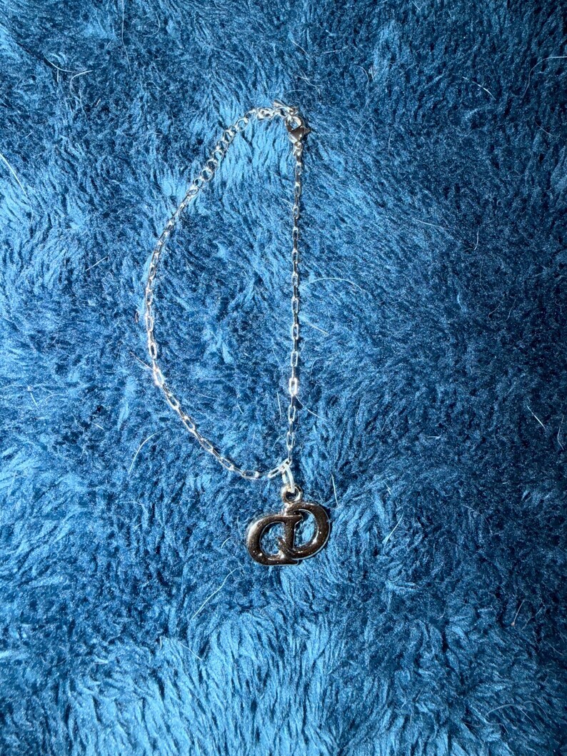 Puede incluir: Una pulsera de cadena de metal en tono plateado que presenta un dije colgante con las letras CD entrelazadas. La delicada cadena de eslabones incluye un peque&ntilde;o cierre de mosquet&oacute;n en el extremo para asegurar este accesorio de mu&ntilde;eca.