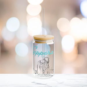 Puede incluir: Un vaso de vidrio transparente con tapa de bambú y pajita de vidrio. El vaso presenta una escritura turquesa que dice "sippora co" y un dibujo lineal de una persona bebiendo de una taza. El vaso está diseñado para bebidas frías.