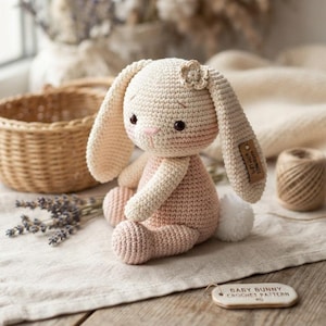 May include: A cream and light pink crocheted bunny toy with long ears, a small flower detail on the head, and a white pom-pom tail. A small brown tag is attached to one ear, and a wooden label reads BABY BUNNY CROCHET PATTERN.