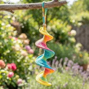 May include: A spiral-shaped crochet hanging ornament featuring a vibrant gradient of yellow, orange, pink, and blue yarn. The decoration includes a small wooden bead at the top and a matching multicolored braided loop for hanging from a branch.