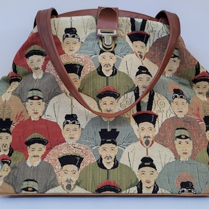 Carpet bag with oriental design and brandy colour leather finishing of metal frame, shoulder straps (ca 60 cms), bottom and strap fastener.