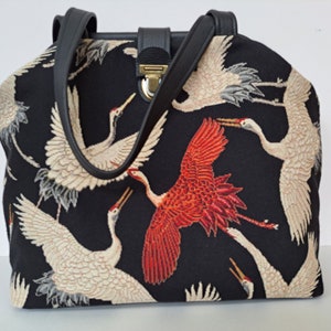Carpet bag made of sturdy black woven fabric with a crane motif. Black leather frame finish, shoulder straps, bottom and strap fastener