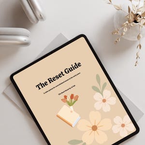 May include: A digital tablet displaying "The Reset Guide" with floral illustrations. The cover text reads "A calm system for overwhelmed moms in the early years." A pair of white headphones and a vase with dried flowers are also visible.
