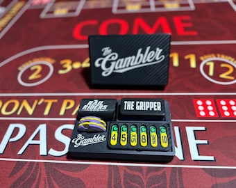 Op de afbeelding: Een zwarte rechthoekige spelaccessoireset met de tekst The Gambler, The Rail Riders en The Gripper. Het bevat een klein dienblad met zes gele rechthoekige markers met de labels 4, 5, SIX, 8, NINE, 10 en een stapel paarse en gele ronde fiches.