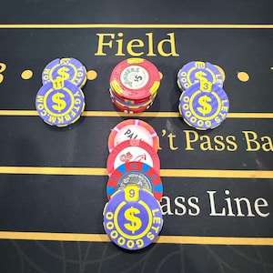 May include: A collection of poker chips in various colors, including blue, red, and yellow, are arranged on a black surface. The chips display dollar signs and text, with the word "Field" visible in the background. Some chips are stacked, while others are placed individually.