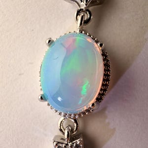 May include: A silver-toned pendant featuring a central oval-shaped iridescent opal cabochon held by four prongs. The setting is accented with two star-shaped charms, one above and one below the opal, both encrusted with small clear stones.