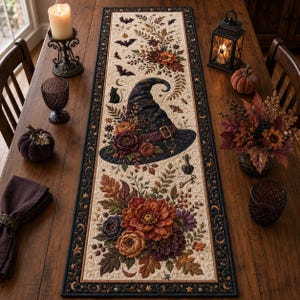 May include: A rectangular table runner featuring a cream-colored center with a dark border. The design includes a central witch hat, a black cat, bats, and floral arrangements in shades of orange, purple, and brown, accented with small stars and moons.