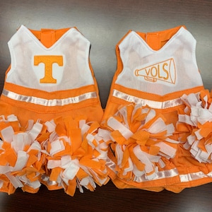 May include: Two orange and white cheerleading outfits with pom-poms. One outfit has a white "T" on the front and the other has a white megaphone with "VOLS" on it.