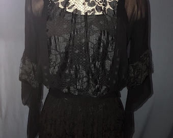 May include: Black vintage dress featuring a sheer, long-sleeved top with lace detailing at the neckline and cuffs. The bodice has a textured design, and the dress includes a long, textured skirt. The dress is a classic piece.