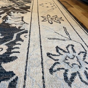 May include: A rectangular area rug featuring a cream-colored base with dark charcoal gray geometric and floral patterns. The design includes a wide border with repeating star-like motifs and linear elements, with the text ARFALRUGS visible.