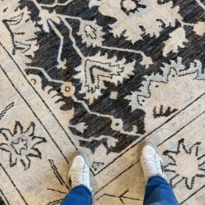 May include: A rectangular area rug featuring a dark charcoal gray and off-white floral pattern with intricate botanical motifs. The design includes a central medallion surrounded by a decorative border with star-like shapes on a light background.