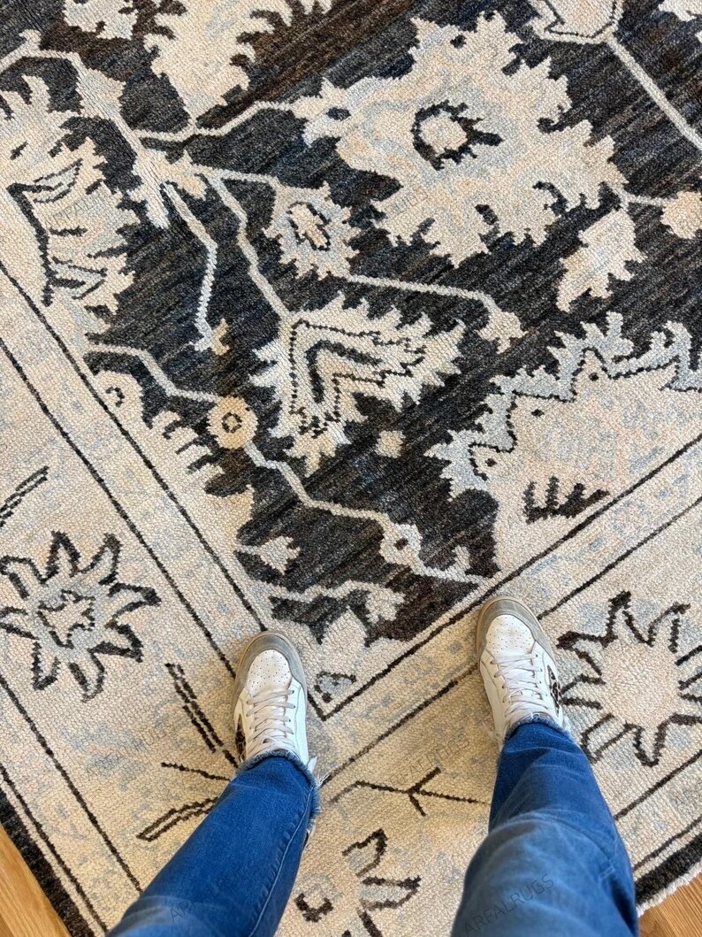 May include: A rectangular area rug featuring a dark charcoal gray and off-white floral pattern with intricate botanical motifs. The design includes a central medallion surrounded by a decorative border with star-like shapes on a light background.