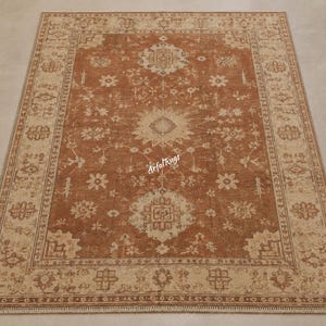 Puede incluir: Una alfombra rectangular de color óxido con un diseño tradicional intrincado. Presenta un medallón central y patrones florales en crema y beige, enmarcados por un borde detallado. Adecuada para salones y dormitorios.