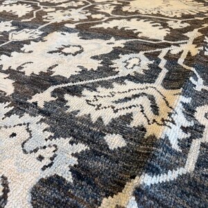 May include: A rectangular area rug featuring a dark charcoal gray and off-white floral pattern. The design consists of repeating large-scale botanical motifs connected by a geometric lattice structure, rendered in a dense, textured pile weave.
