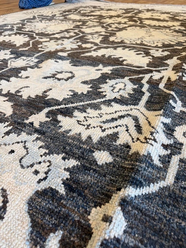 May include: A rectangular area rug featuring a dark charcoal gray and off-white floral pattern. The design consists of repeating large-scale botanical motifs connected by a geometric lattice structure, rendered in a dense, textured pile weave.