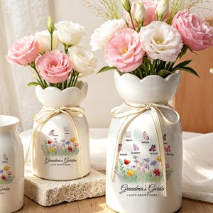 May include: A white ceramic mug and two white ceramic vases with scalloped rims, each featuring a colourful floral graphic, butterflies, and the printed text Grandma's Garden Love Grows Here, with the vases tied with cream-coloured ribbons.