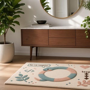 Peut inclure: Un tapis rectangulaire de couleur cr&egrave;me pr&eacute;sentant un serpent bleu et rose formant un cercle au centre. Le motif inclut le texte "for i in range(n):", "loop:", un symbole de crochet de code, un c&oelig;ur et deux brins de feuilles bleus et roses.