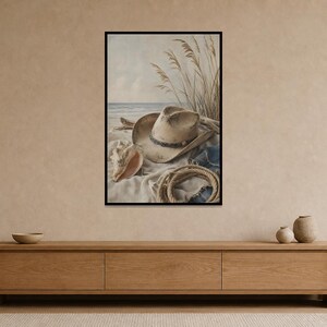 May include: A framed print depicting a beach scene with a cowboy hat, seashell, and rope. The artwork features a neutral color palette with a beige hat, a light blue ocean, and beige sand. The image evokes a coastal, rustic theme.