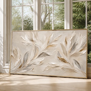 Puede incluir: Una pieza de arte mural rectangular que presenta una pintura texturizada de estilo impasto de hojas abstractas en tonos crema, beige, blanco y oro metálico. La obra está encerrada en un marco de madera de color claro con trazos gruesos.