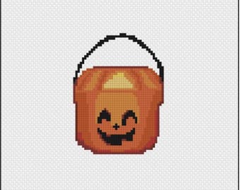 Może przedstawiać: Wzór do haftu krzyżykowego w stylu pixel art przedstawiający wiaderko na cukierki w kształcie dyni. Dynia jest pomarańczowa z czarnym uchwytem i wyciętą twarzą z dwoma trójkątnymi oczami oraz poszarpanymi ustami na białym tle w kratkę.