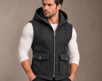 Op de afbeelding: Een antracietgrijze vest met capuchon, voorzien van een zilverkleurige ritssluiting over de gehele lengte, twee voorzakken met klep en metalen drukknopen, en verticale naden. Gedragen over een wit shirt met lange mouwen.