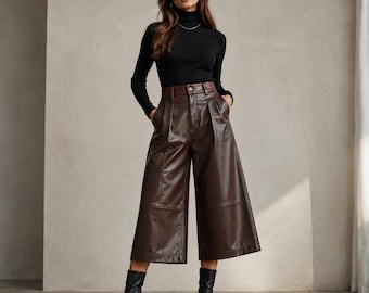 Op de afbeelding: Een vrouw draagt een zwarte coltrui, een bruine leren culotte, een bruine riem en zwarte enkellaarsjes met hakken. De culotte heeft een wijde pijp en een hoge taille. De outfit is een stijlvol ensemble.