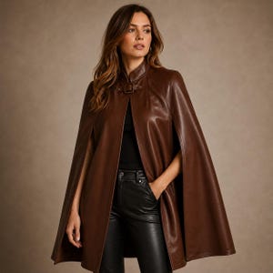 May include: A dark brown leather cape featuring a high collar and a front buckle closure. The garment has an open-front design with arm slits, providing a structured silhouette. It is worn over a black top and black leather trousers.